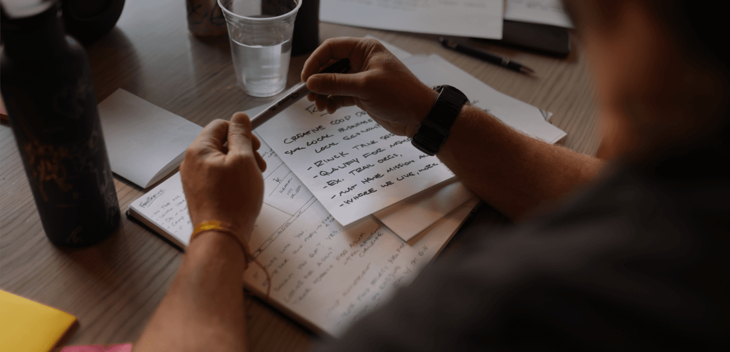 Person holding pen with pad of paper visible on table